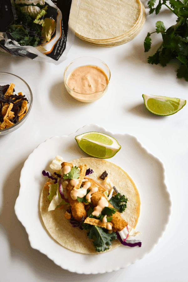 A fish stick taco on a white plate surrounded by fixings.