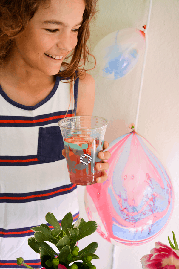 Boy holding strawberry lemonade in a clear plastic party cup next to balloons.