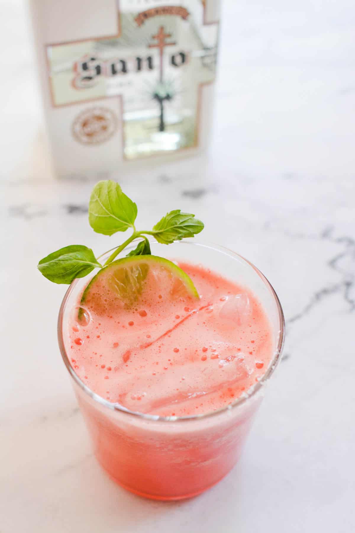 Overhead shot of a short cocktail glass with a watermelon margarita next to a bottle of tequila.