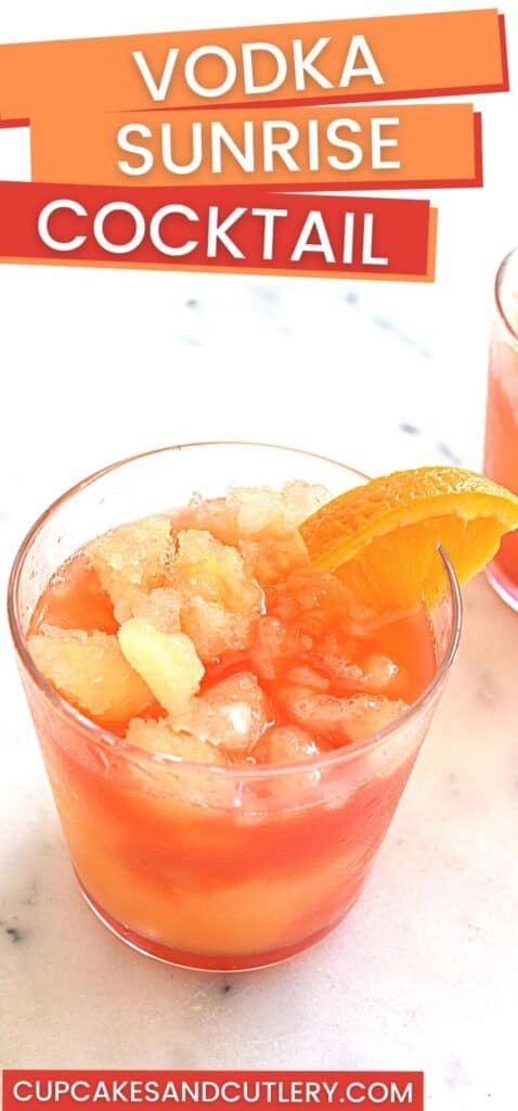 An orange and red slushie cocktail on a table with an orange slice garnish.