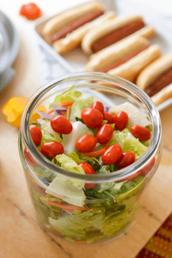 A simple green salad side dish served in a large glass jar for a party.