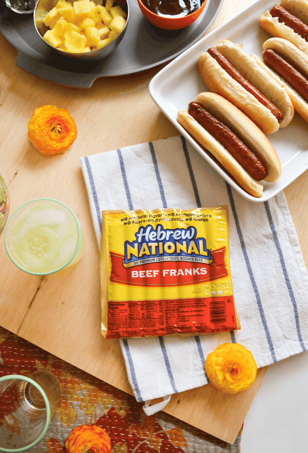 A package of Hebrew National hot dogs on a table next to hot dogs in buns on a white plate.