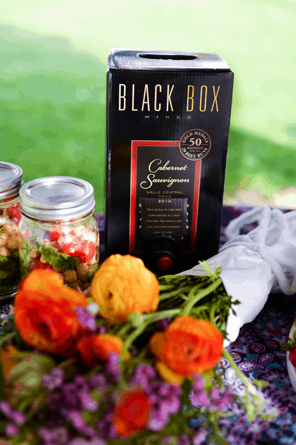 A party table out in a park with food and a box of Black Box wine. 