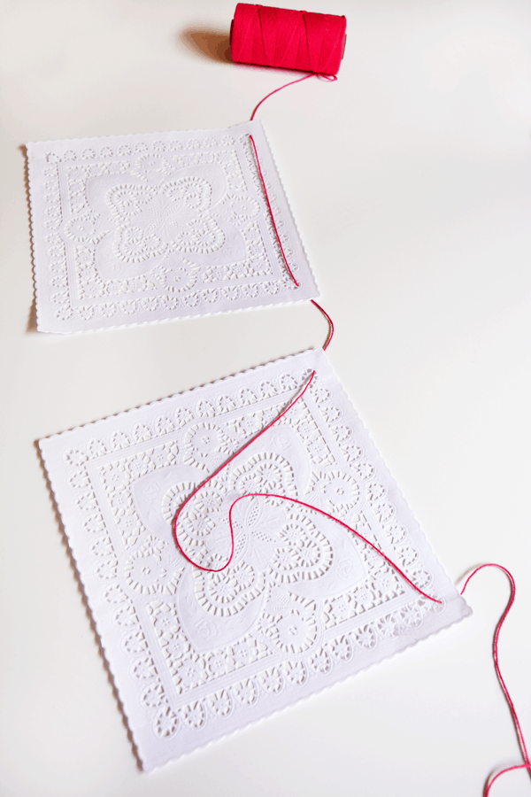 White doilies laying on a white table being strung on a bright pink string.