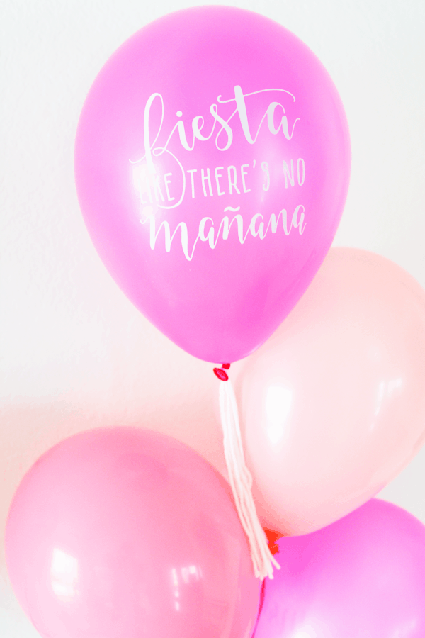Hot pink balloon that says 'fiesta like there's no tomorrow" on a string with a white yarn tassel and other pink balloons.