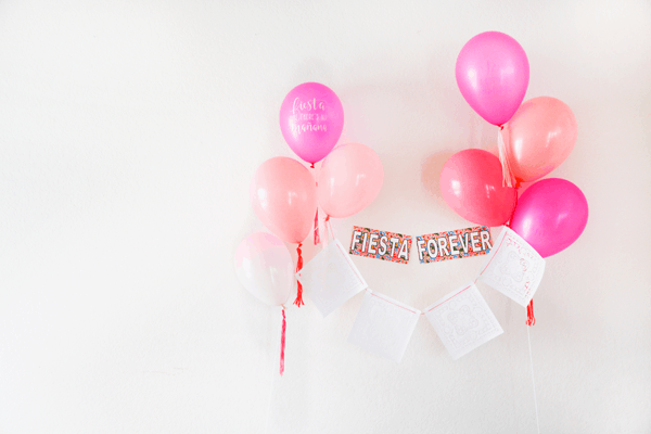 Balloons in a variety of pink colors holding up a papel picado style banner and a party sign that says "fiesta forever".