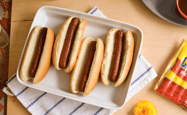 4 hot dogs in buns on a white plate on a bbq party table.
