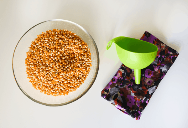 Top down image of a bowl of popcorn, a funnel, and an empty DIY freezer bag.
