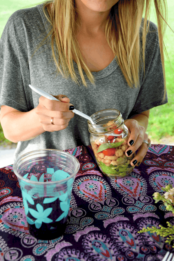 A woman eating a White Bean Caprese Salad out of a Mason jar at an outdoor table. 