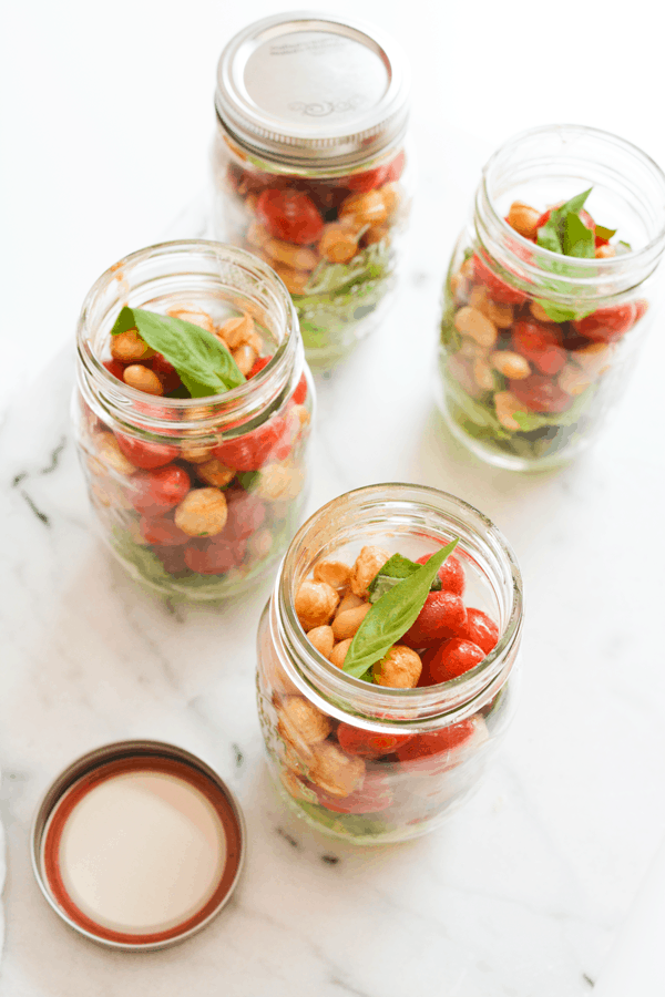 Individual white bean caprese salads in mason jars on a table. 