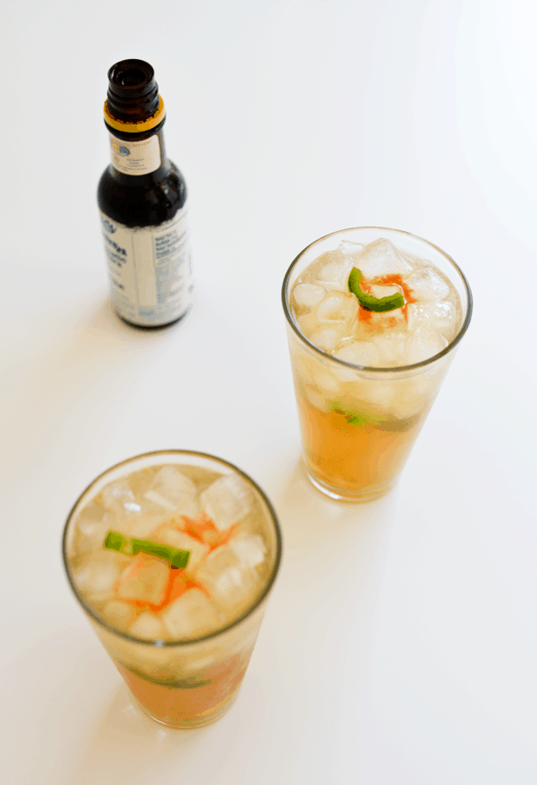 2 Mexican Mule cocktails with jalapeno in glasses with ice next to a bottle of cocktail bitters.