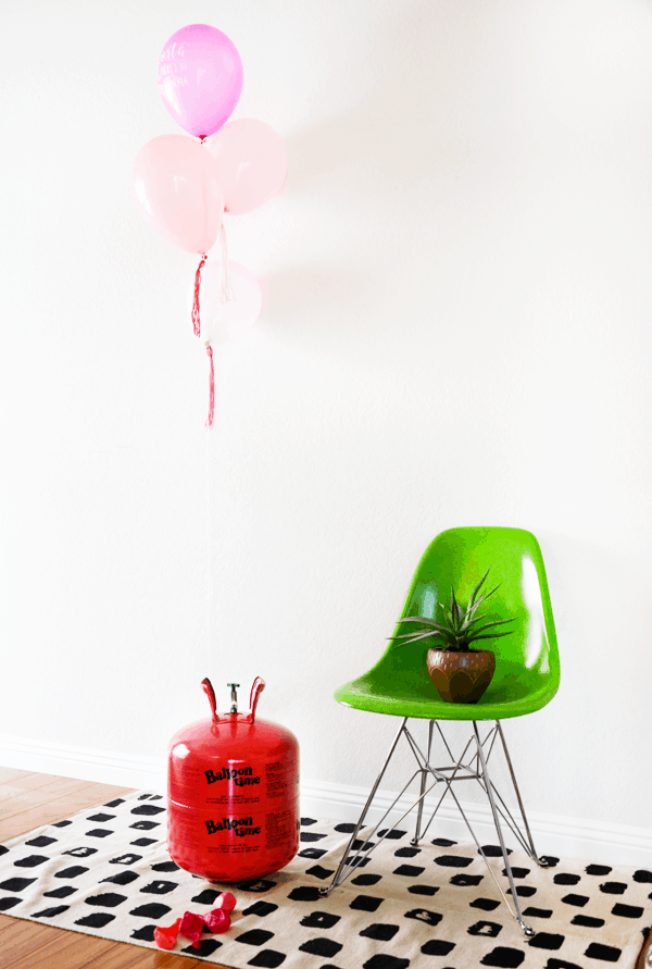 W bright green chair with a plant on it next to a Balloon Time Helium tank and a floating string with 4 pink balloons. 
