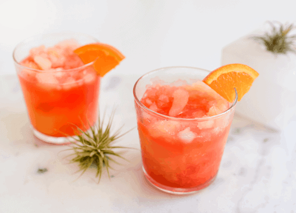 2 cocktail glasses with a vodka sunrise cocktail that looks like an orange and red slushie.