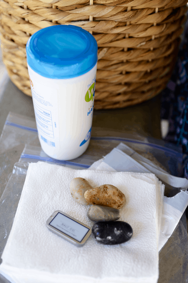 A container of hand wipes, rocks and a small container of salt on top of napkins and plastic storage bags. 