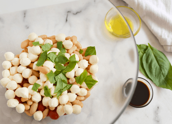 Ingredients for a caprese salad with white beans in a glass bowl. 