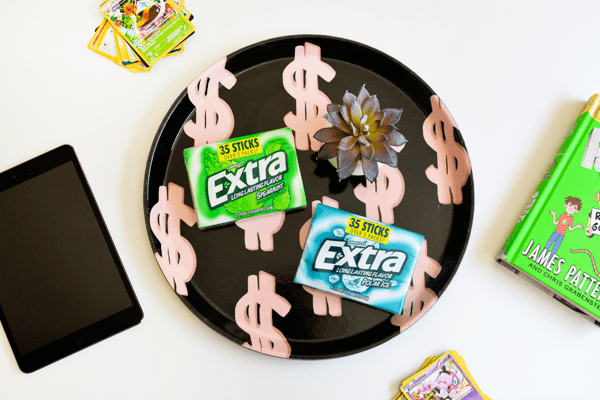 A tray with dollar signs on it and two packs of Extra gum. 