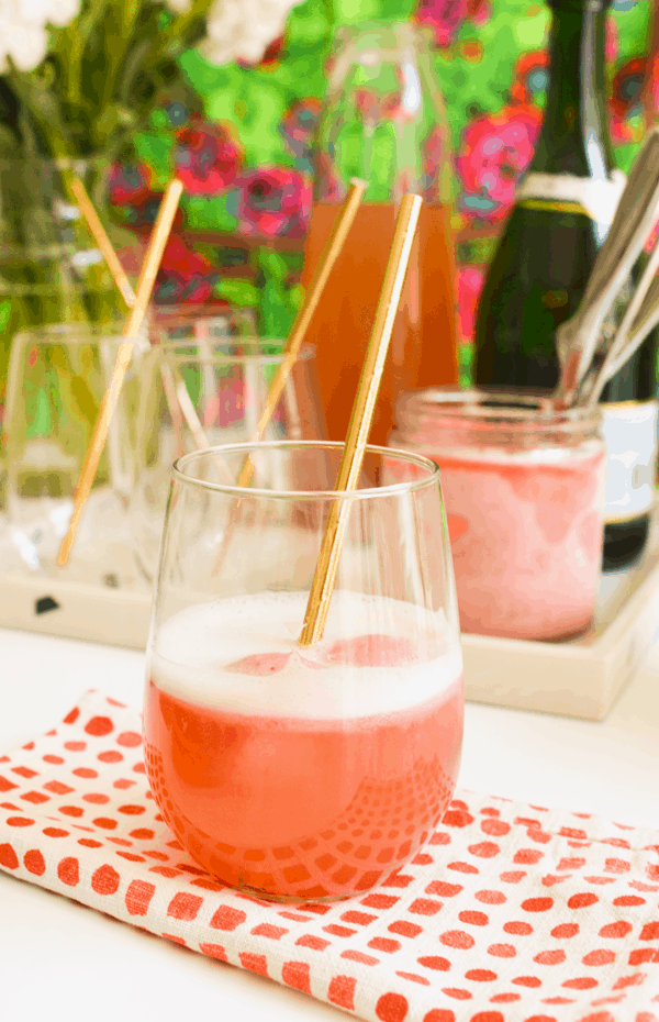 A delicious strawberry champagne float in a stemless wine glass with a copper straw sitting on top of a red and white cloth napkin.