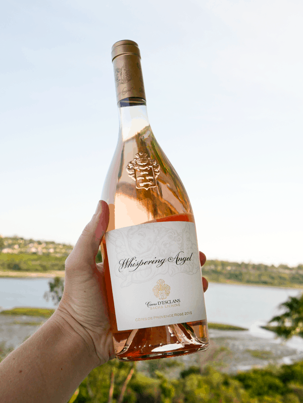 A hand holding up a bottle of Whispering Angel rose.