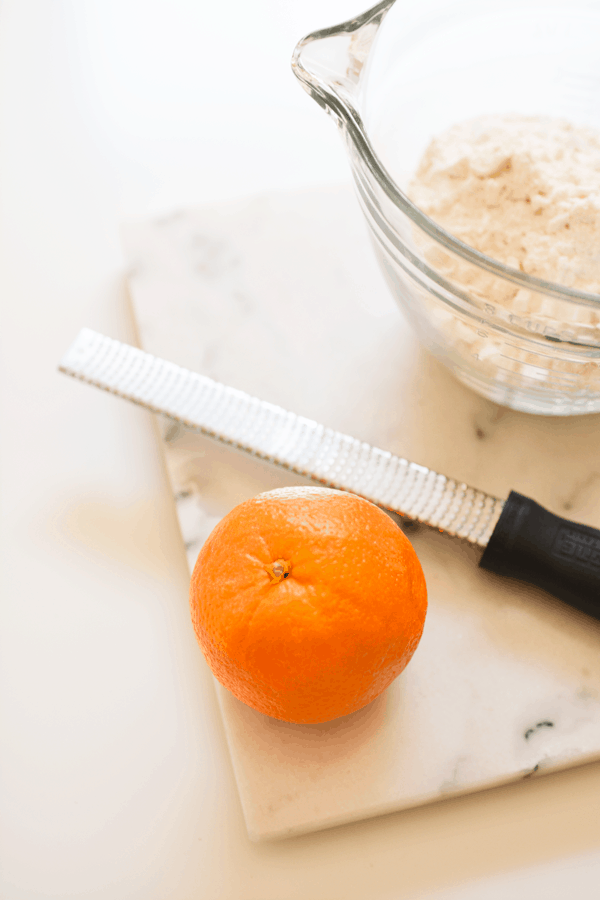 A bowl of cookie batter next to an orange and a citrus zester. 