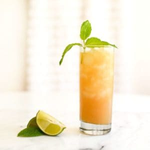 An Apple Juice mojito in a glass with mint garnish and mint and lime next to it.