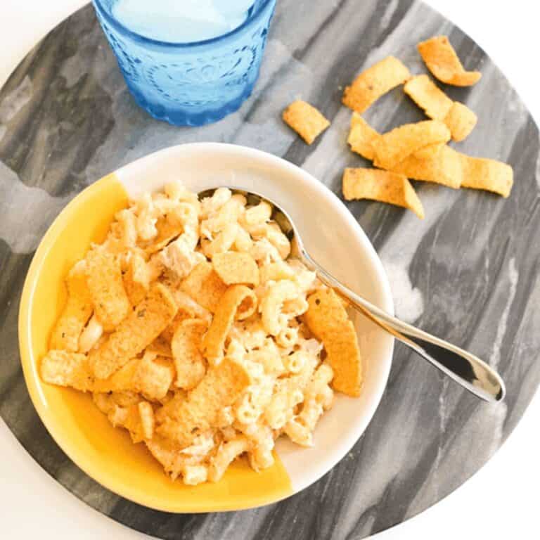 A yellow and white bowl of tuna and noodles topped with corn chips.