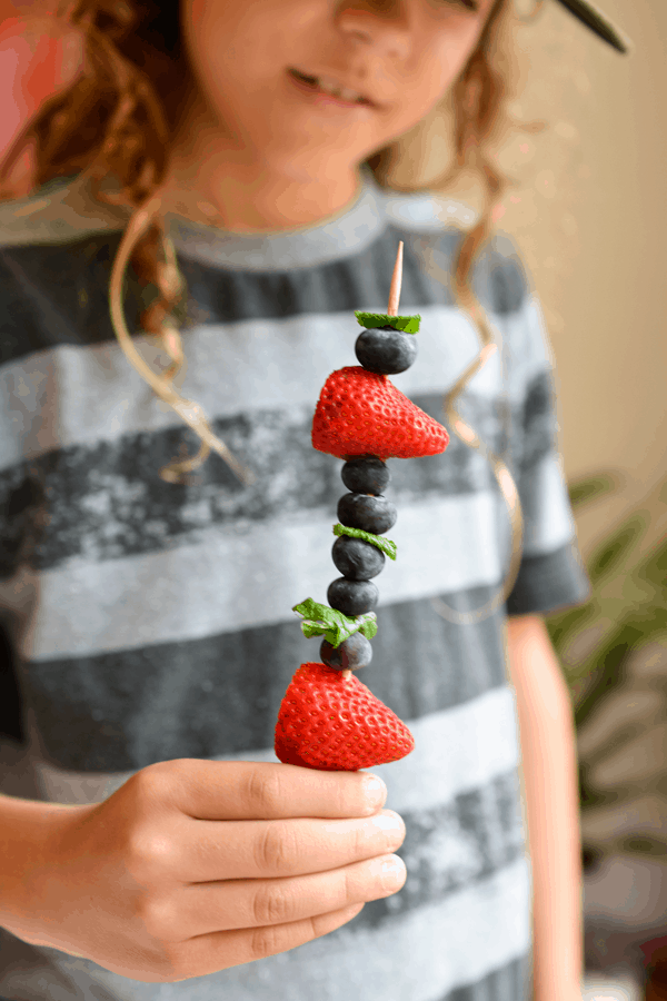 Kid holding a skewer with fresh mint and fruit. 