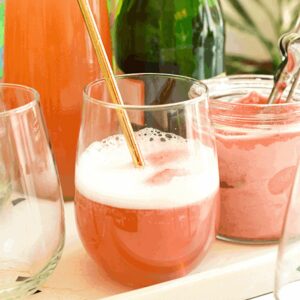 Two glasses, one filled with a champagne float, in front of the ingredients to make a strawberry sorbet cocktail.