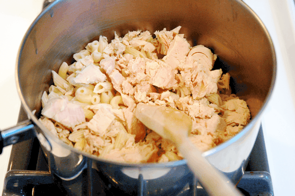 A saucepan with cooked elbow noodles and tuna from a can being mixed in. 