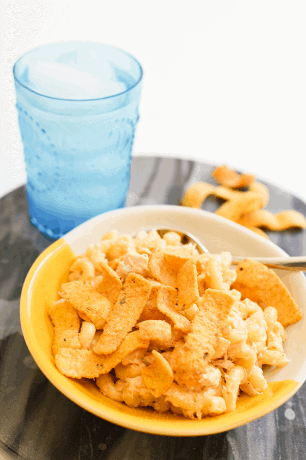 A bowl on a table with elbow noodles mixed with tuna and mayo and topped with corn chips. 