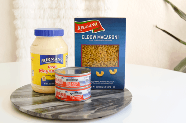 A tray on a table with a jar of mayonnaise, a box of elbow macaroni and 2 cans of tuna. 