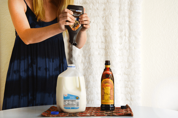 Woman adding chocolate syrup to a milk jug.