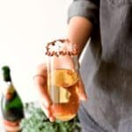 Close up of a woman holding a stemless champagne flute in her hand that has been rimmed with dried rose petals.