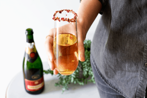 Woman holding a champagne flute with a dried rose petal rim. 