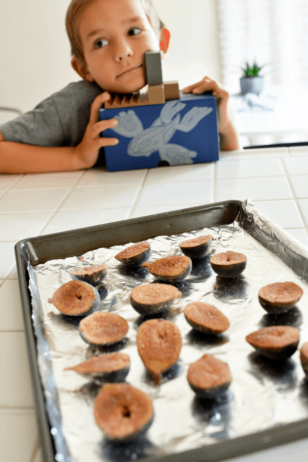 A baking sheet full of figs in front of a child waiting for dessert.