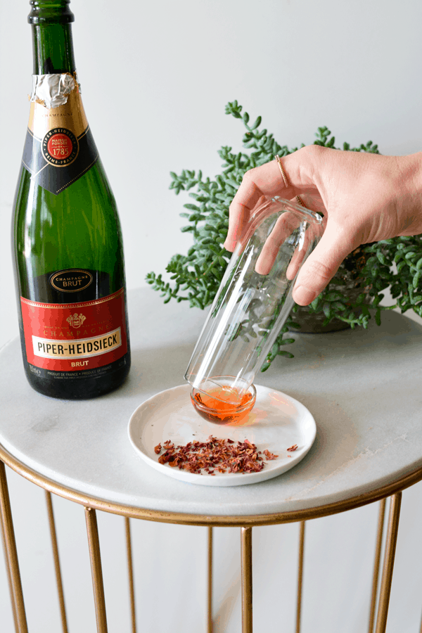 Woman dipping a stemless champagne flute in a small bowl of rose syrup. 