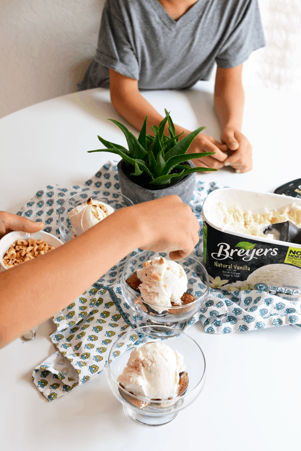 Two boys putting toasted hazelnuts on top of bowls of roasted figs topped with vanilla ice cream.