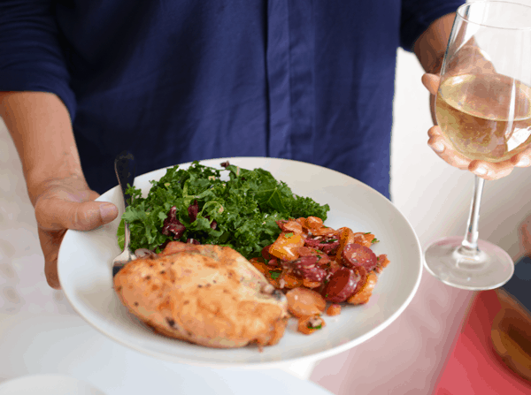 Woman holding a plate in one hand full of yummy food and a glass of wine in the other hand. 