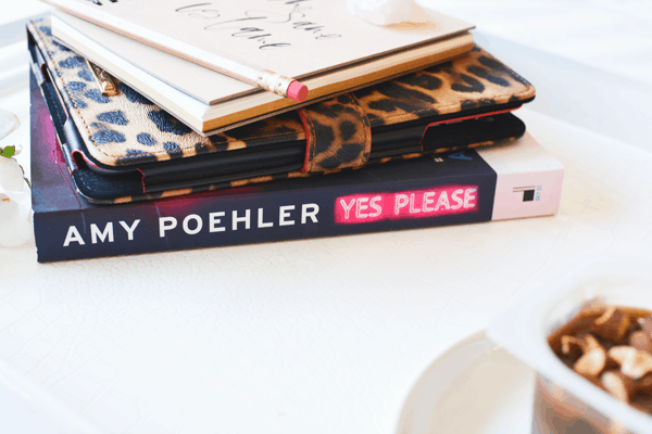 A book by Amy Poehler, an ipad and a notebook stacked up on a tray. 