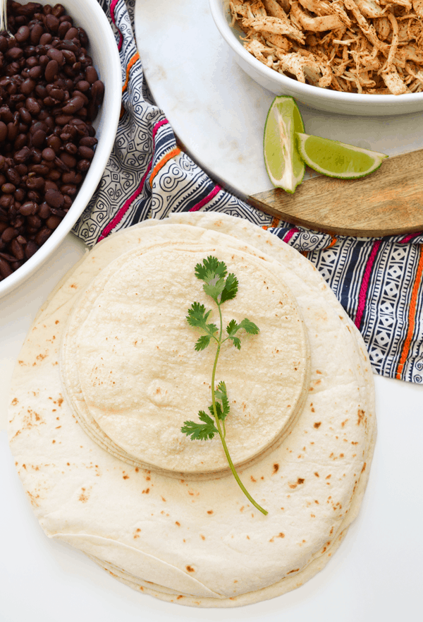 Stacks of corn and flour tortillas on a table with a sprig of cilantro.