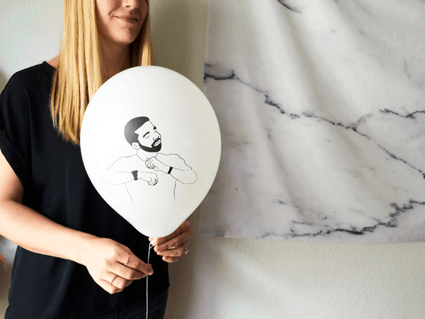 Woman holding a white balloon with Drake on it.