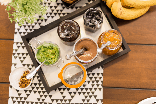 A tray holding a variety of jams, smashed avocado and nut butters for a brunch.