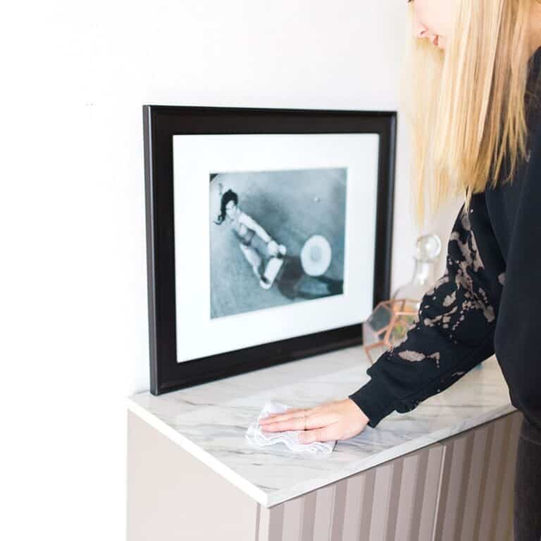 Woman in black sweatshirt cleaning a small marble topped table.