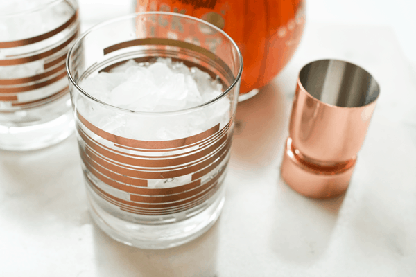 Cocktail glasses with crushed ice on a table next to a bottle and jigger.