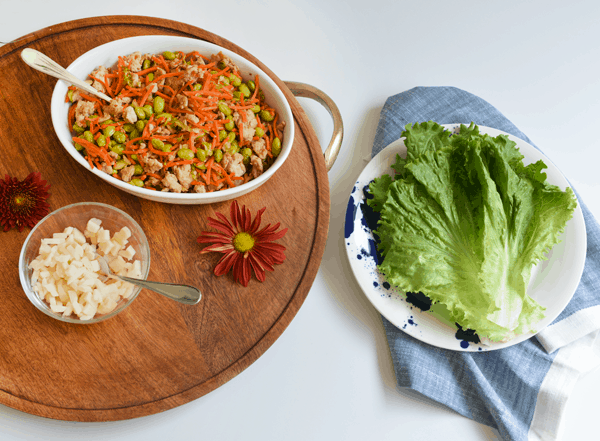 Wooden tray with plate of lettuce leaves next to a bowl for a ground turkey dinner recipe.
