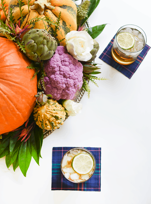 Overhead view of a fall centerpiece with vegetables and pumpkins next to glasses holding a Pumpkin Mule on coasters.