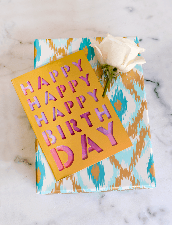 A wrapped gift with a happy birthday card and white rose on top. 