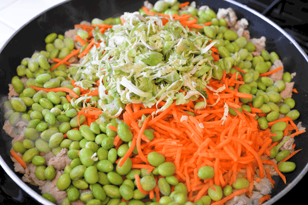 Ground turkey, edamame, shredded carrots and green onions in a pan for a teriyaki ground turkey stir fry.