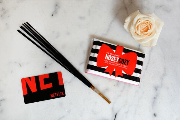 A bundle of incense, a pack of tissues, a rose and a Netflix gift card on a table. 