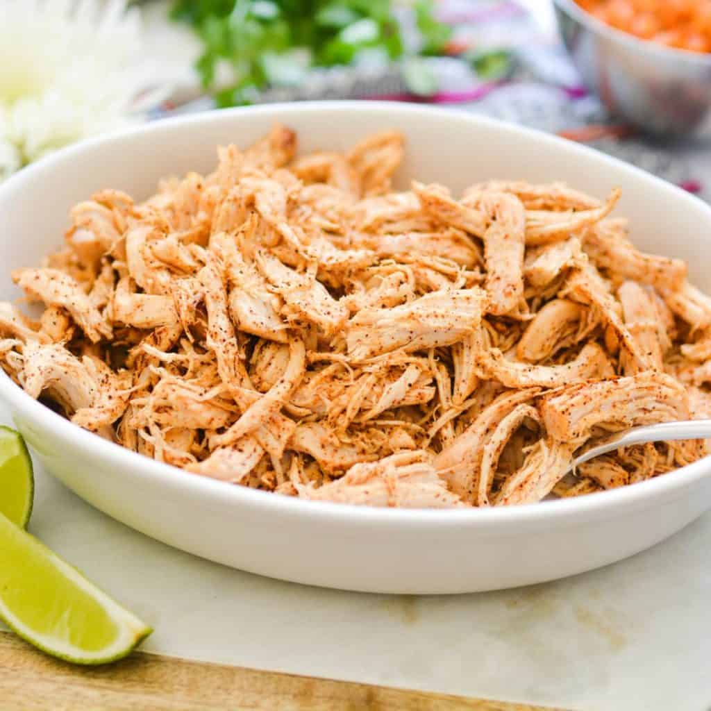Shredded chicken seasoned with taco seasonings in a white bowl.