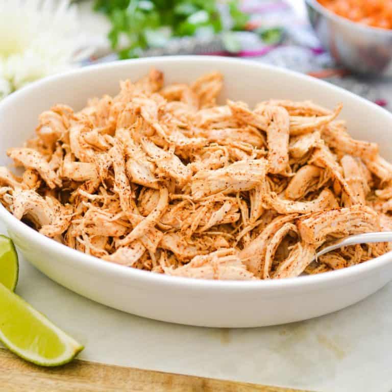 Shredded chicken seasoned with taco seasonings in a white bowl.